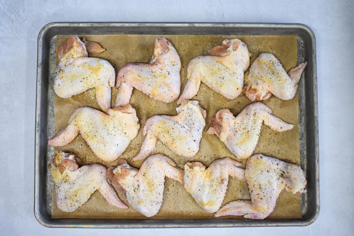 Raw chicken wings arranged on a baking sheet lined with a cooling rack.