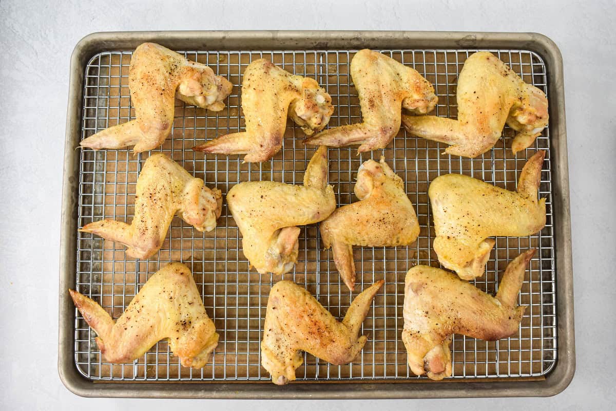 Baked chicken wings arranged on a baking sheet lined with a cooling rack.