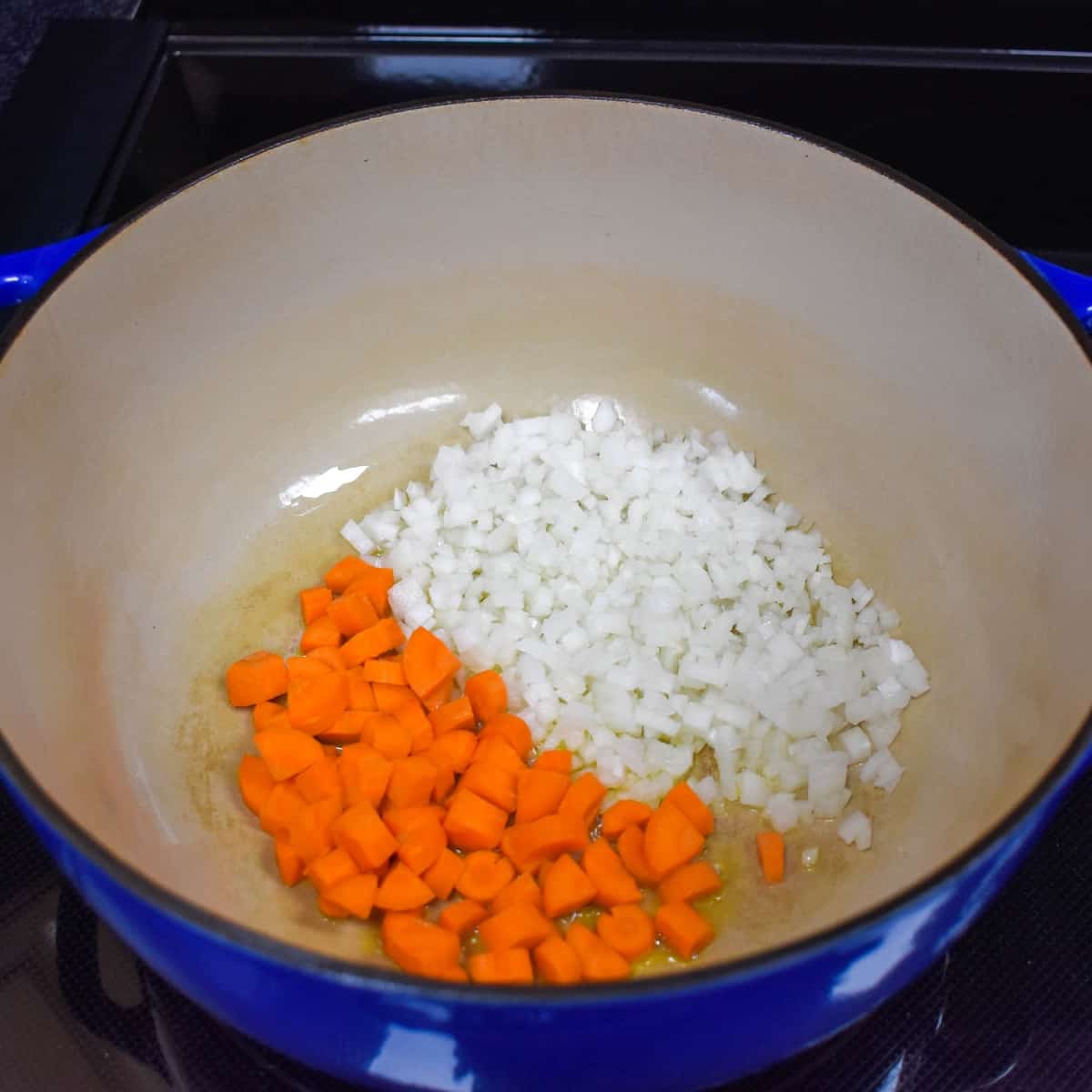An image of diced onions and carrots in a large blue pot.