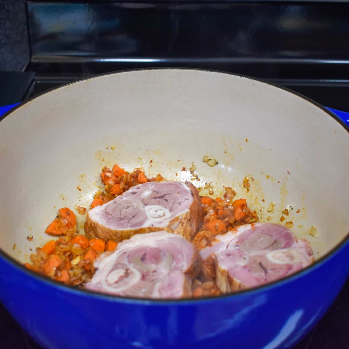 An image of three sliced ham shank pieces on cooked vegetables in a large blue pot.
