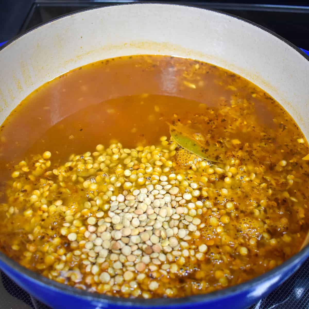 Lentils added to the broth in a large pot.