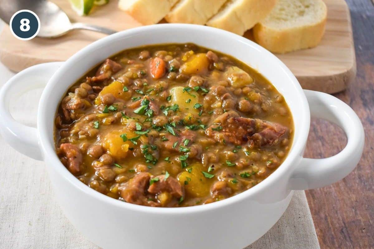 Finished potaje de lentejas served in a white bowl with ham, lentils, potatoes, and pumpkin.