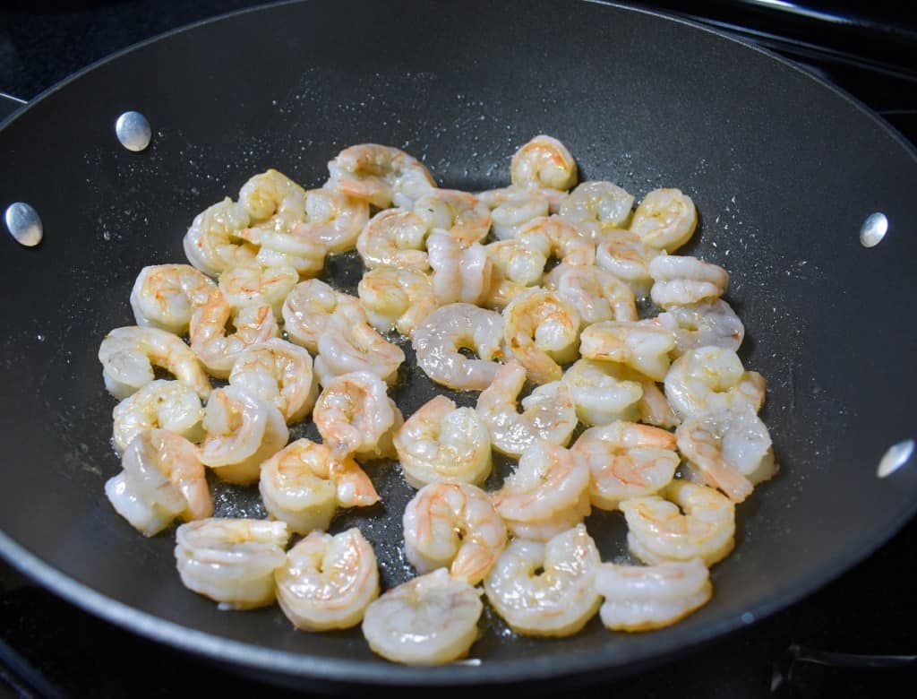Shrimp cooking in a large, black skillet.