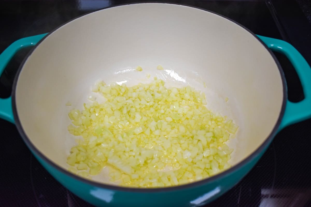 Sautéed onions in olive oil in a large white and aqua pot.