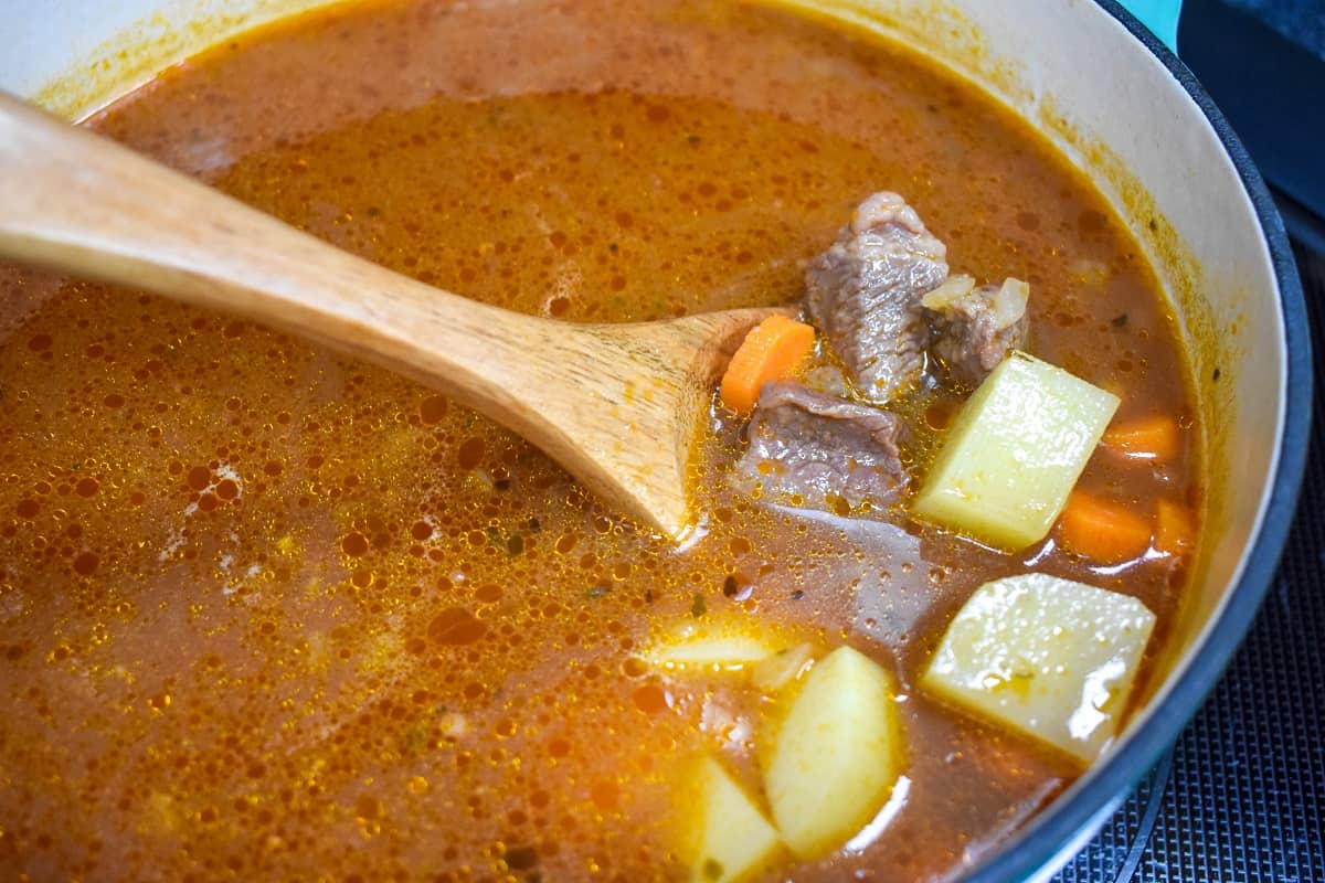 A wooden spoon showing potatoes and carrots added to the beef soup.