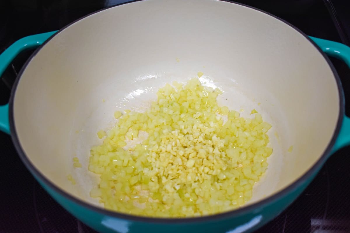 Minced garlic added to the sautéed onions in a white and aqua pot.