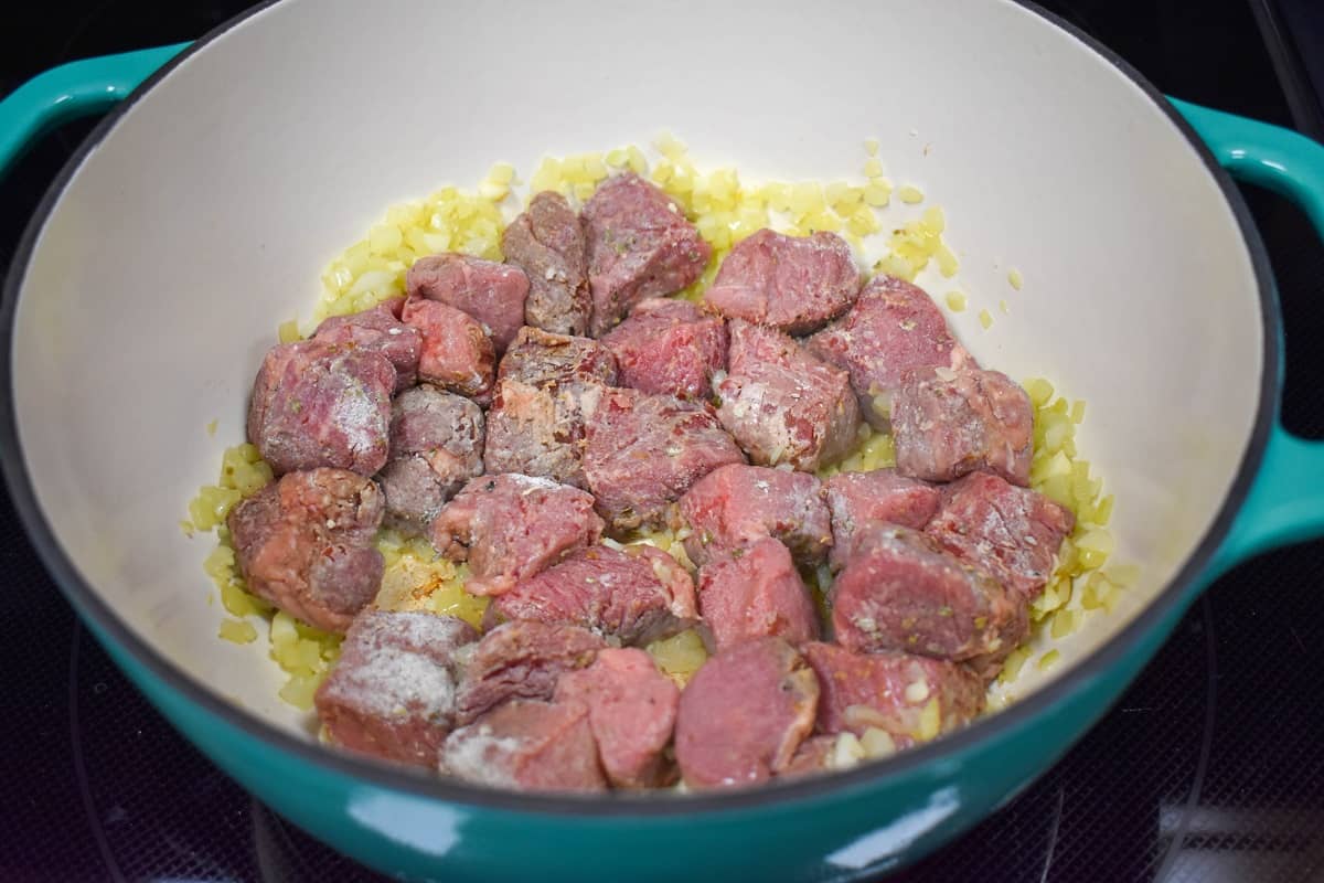 Beef chunks being browned in a large white and aqua pot.