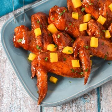 Mango habanero wings arranged on a blue platter and garnished with diced mango and parsley.