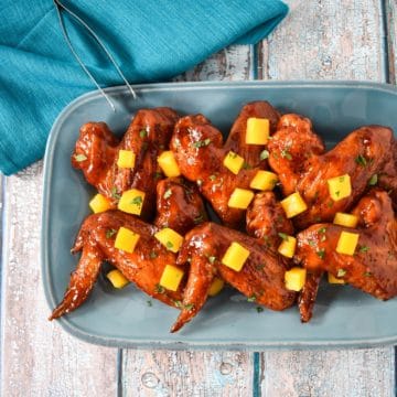 A blue platter with the wings arranged on them garnished with diced mango and chopped parsley.