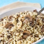 An image of the mushroom rice pilaf served in a white bowl with a beige linen and set on a light blue table.
