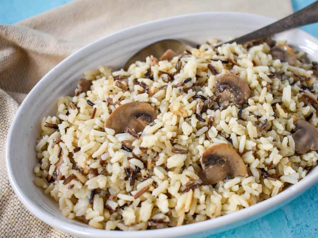 An image of the mushroom rice pilaf served in a white bowl with a beige linen and set on a light blue table.