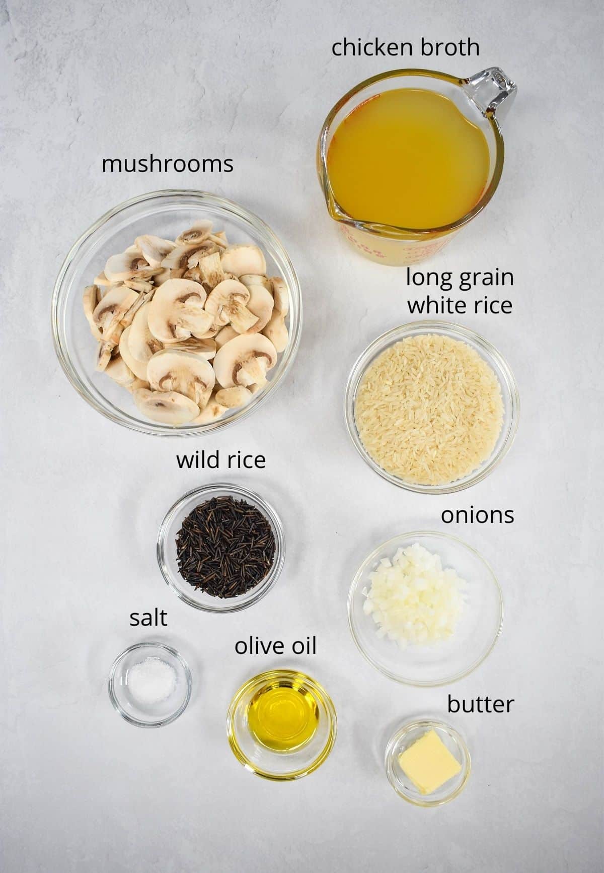 The ingredients for the rice dish, prepped and separated in glass bowls, displayed on a white table. Each ingredient is labeled in small black letters.