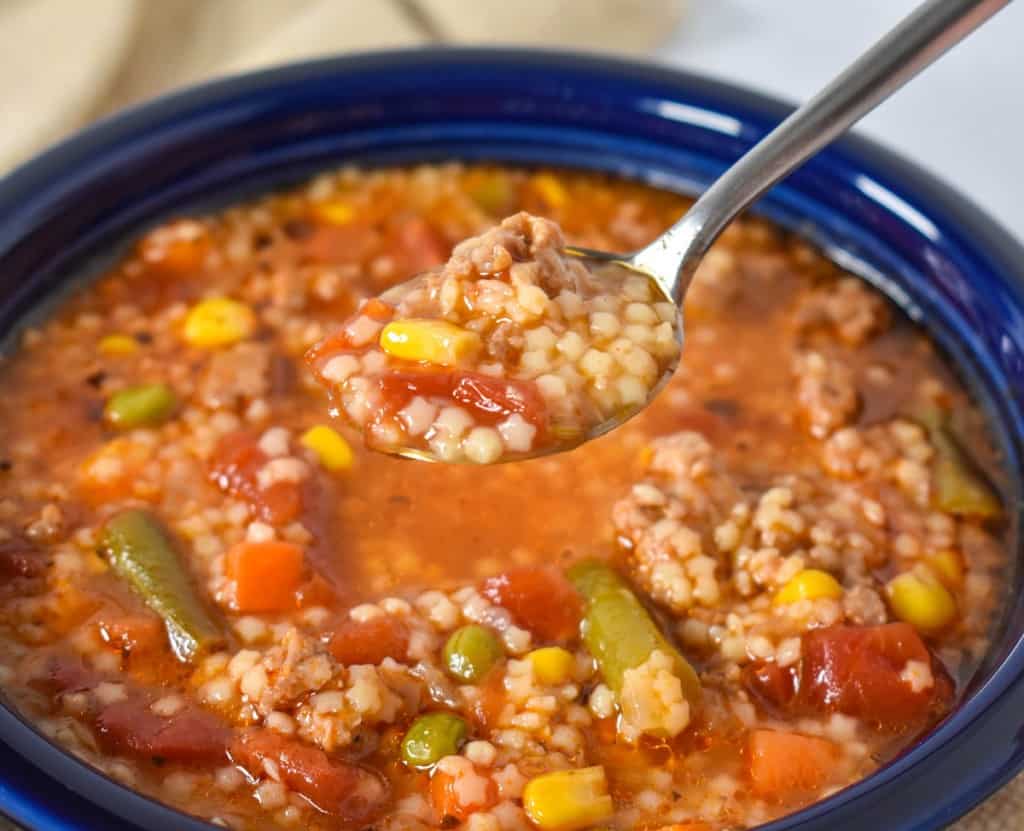 An image of a spoonful of the pastina soup over a blue bowl where it is served.