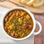 The potaje de lentejas (Cuban lentil soup) served in a white bowl and served with sliced bread.