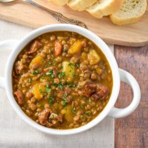 The potaje de lentejas (Cuban lentil soup) served in a white bowl and served with sliced bread.