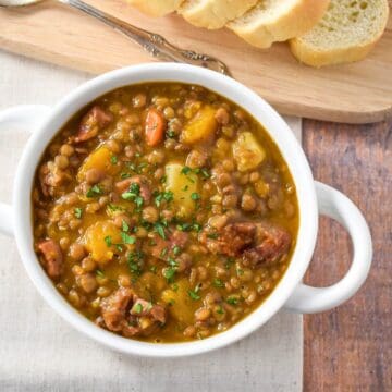 The potaje de lentejas (Cuban lentil soup) served in a white bowl and served with sliced bread.