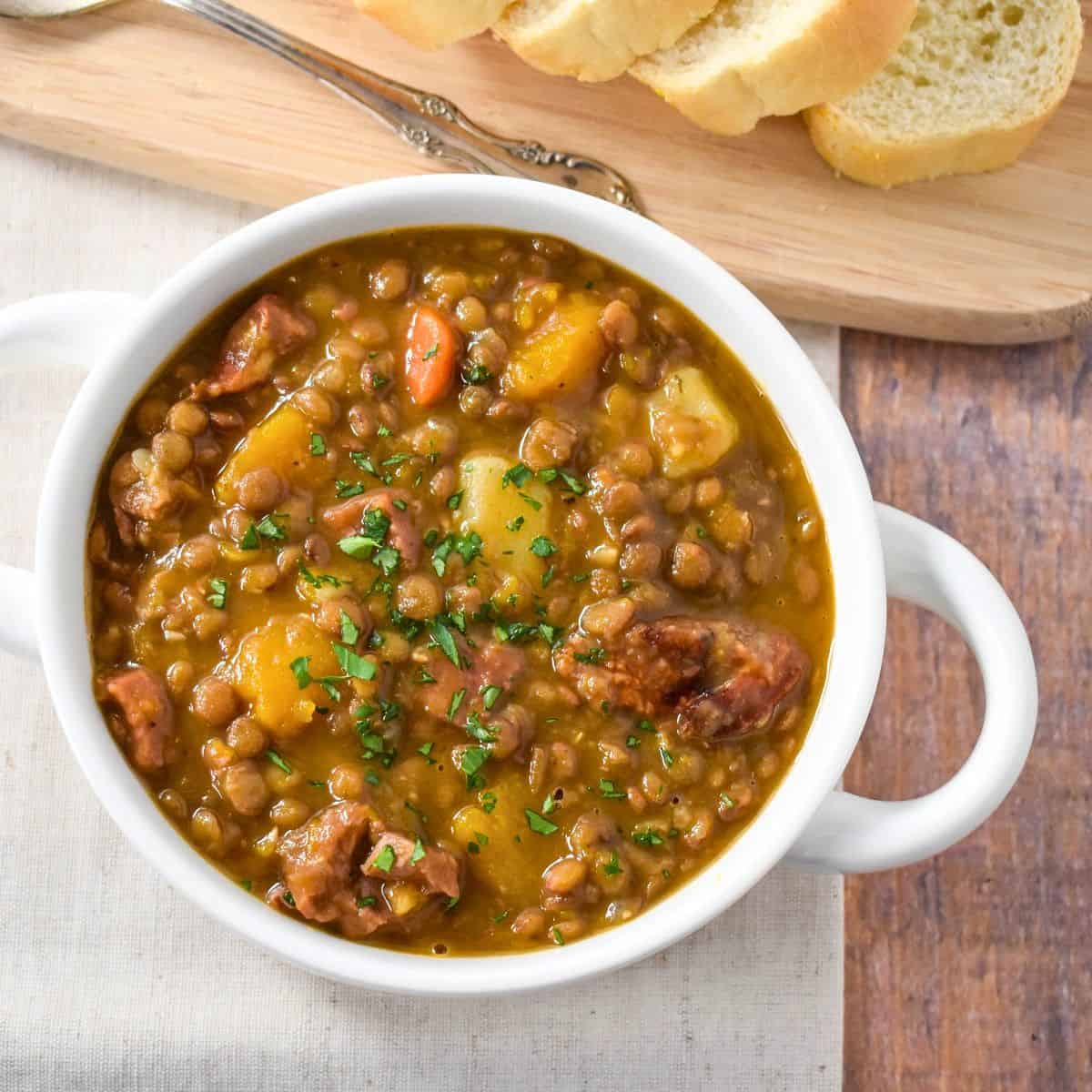 The potaje de lentejas (Cuban lentil soup) served in a white bowl and served with sliced bread.