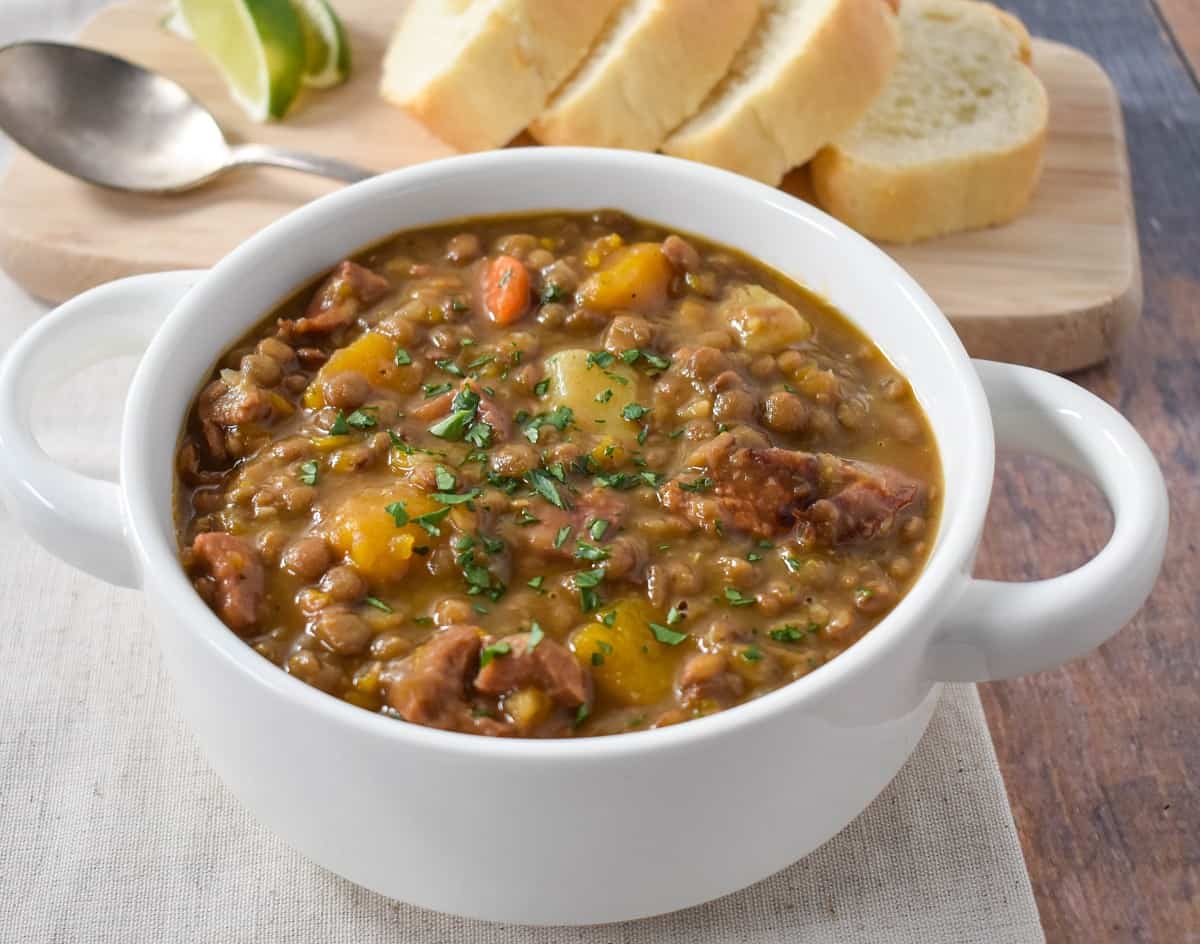 The lentil soup served in a white bowl with sliced bread and lime wedges in the background.