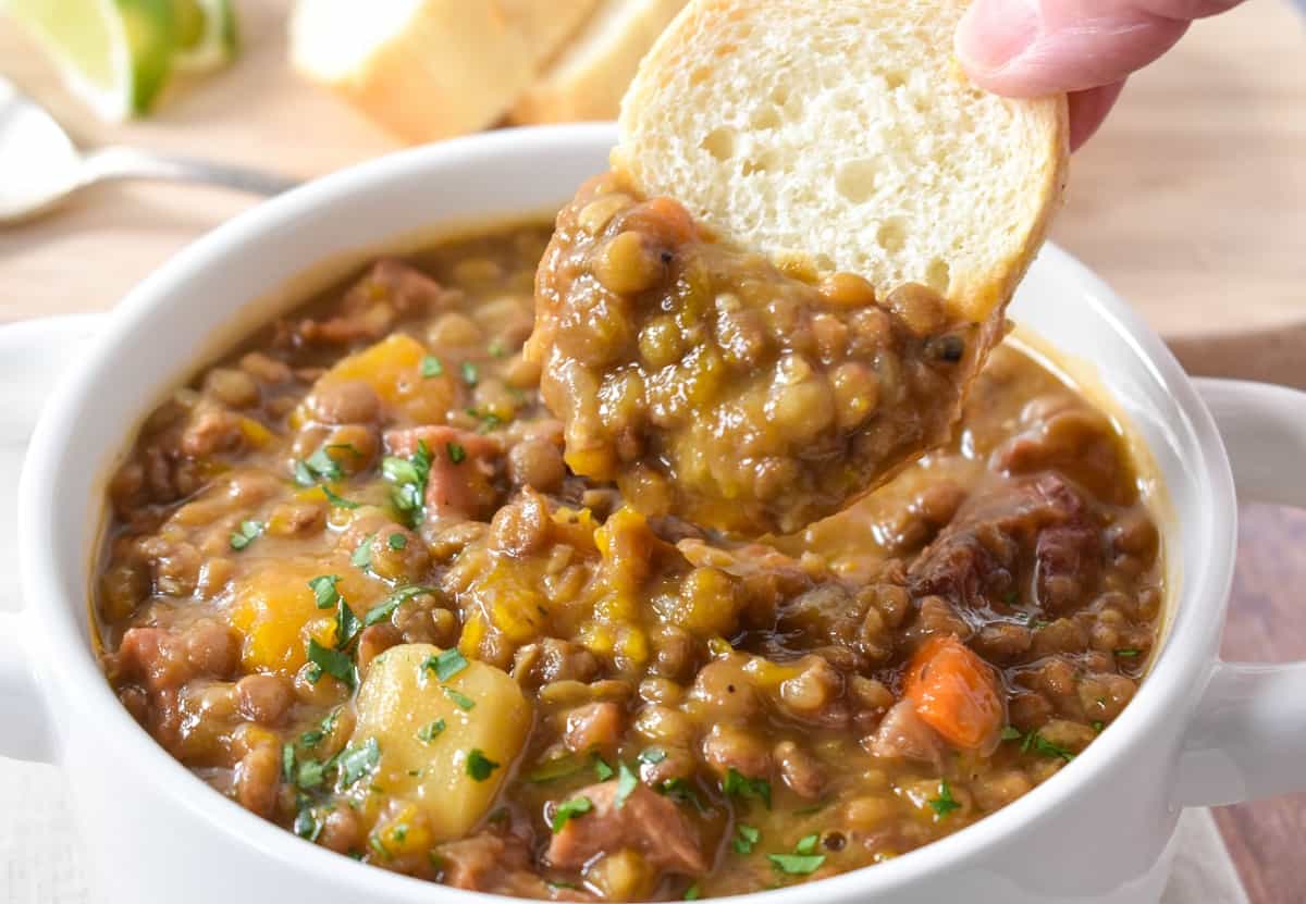 A close up image of the potaje de lentejas being scooped with a slice of baguette bread.