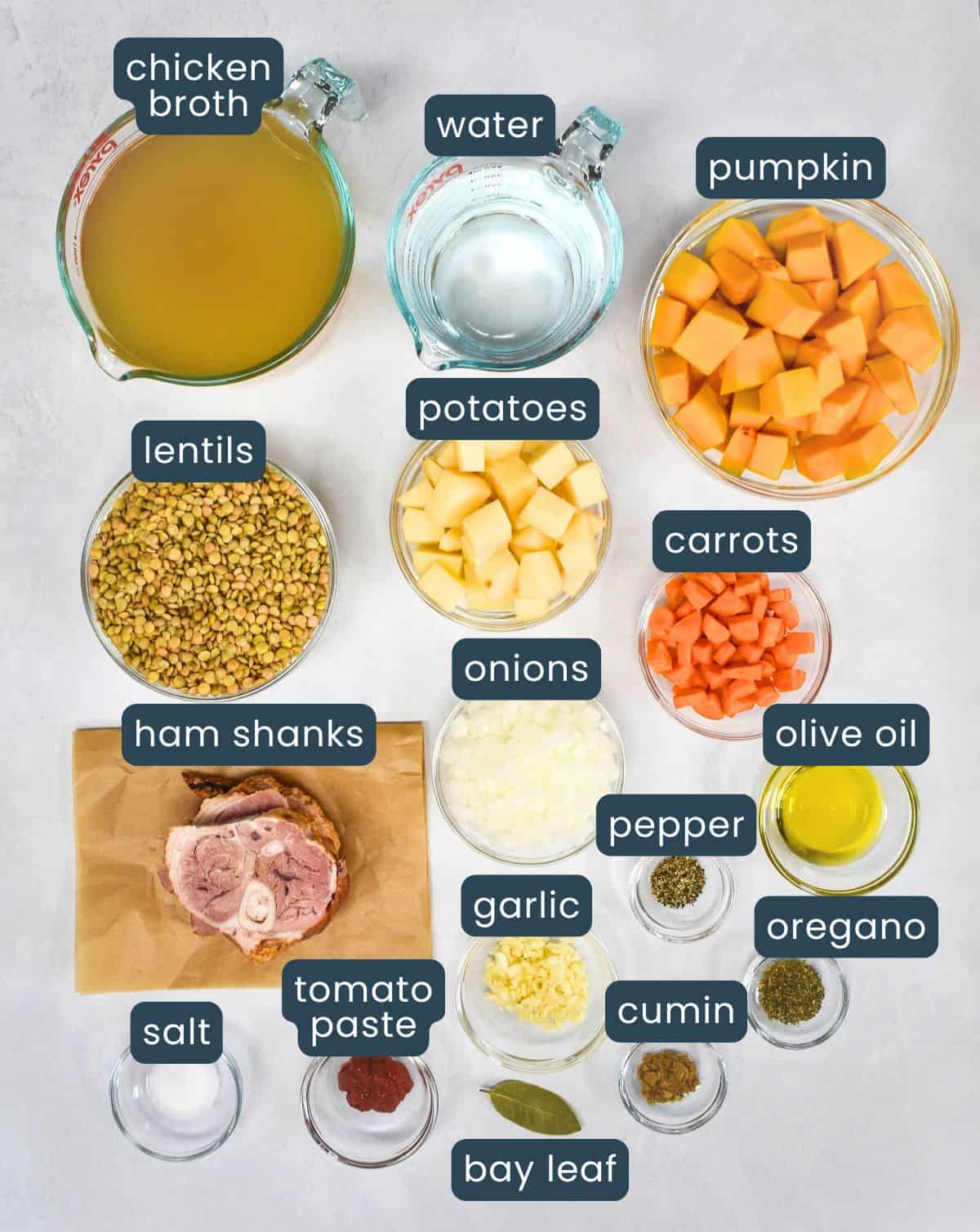 The ingredients for the potaje de lentejas arranged in glass bowls on a white table, with each labeled.