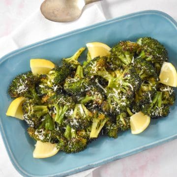 The roasted broccoli served on a light blue platter and garnished with grated parmesan and lemon wedges.