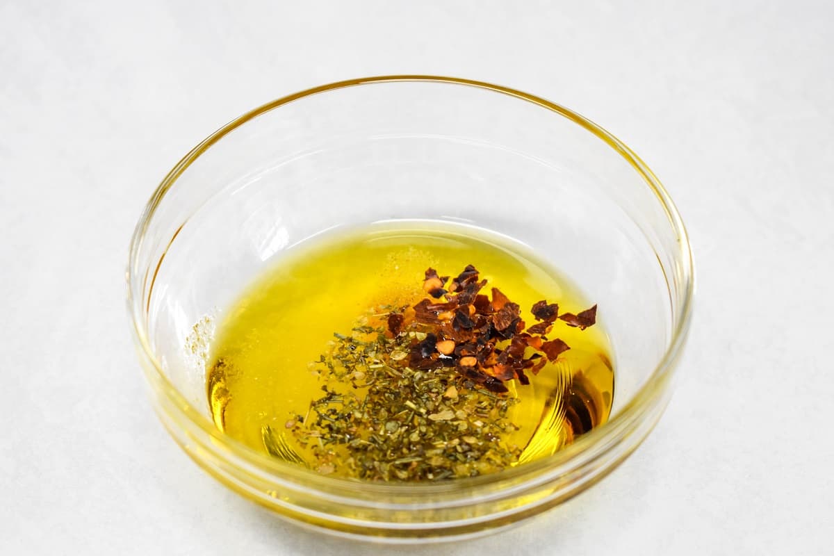 Olive oil and spices in a small, glass bowl set on a white table.