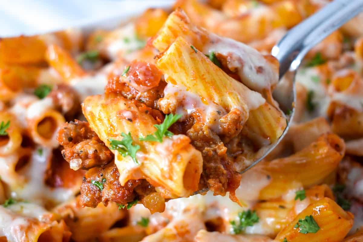 The finished pasta being held over the casserole dish with a large serving spoon.