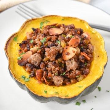 An image of the sausage stuffed acorn squash garnished with chopped parsley and served on a white plate.