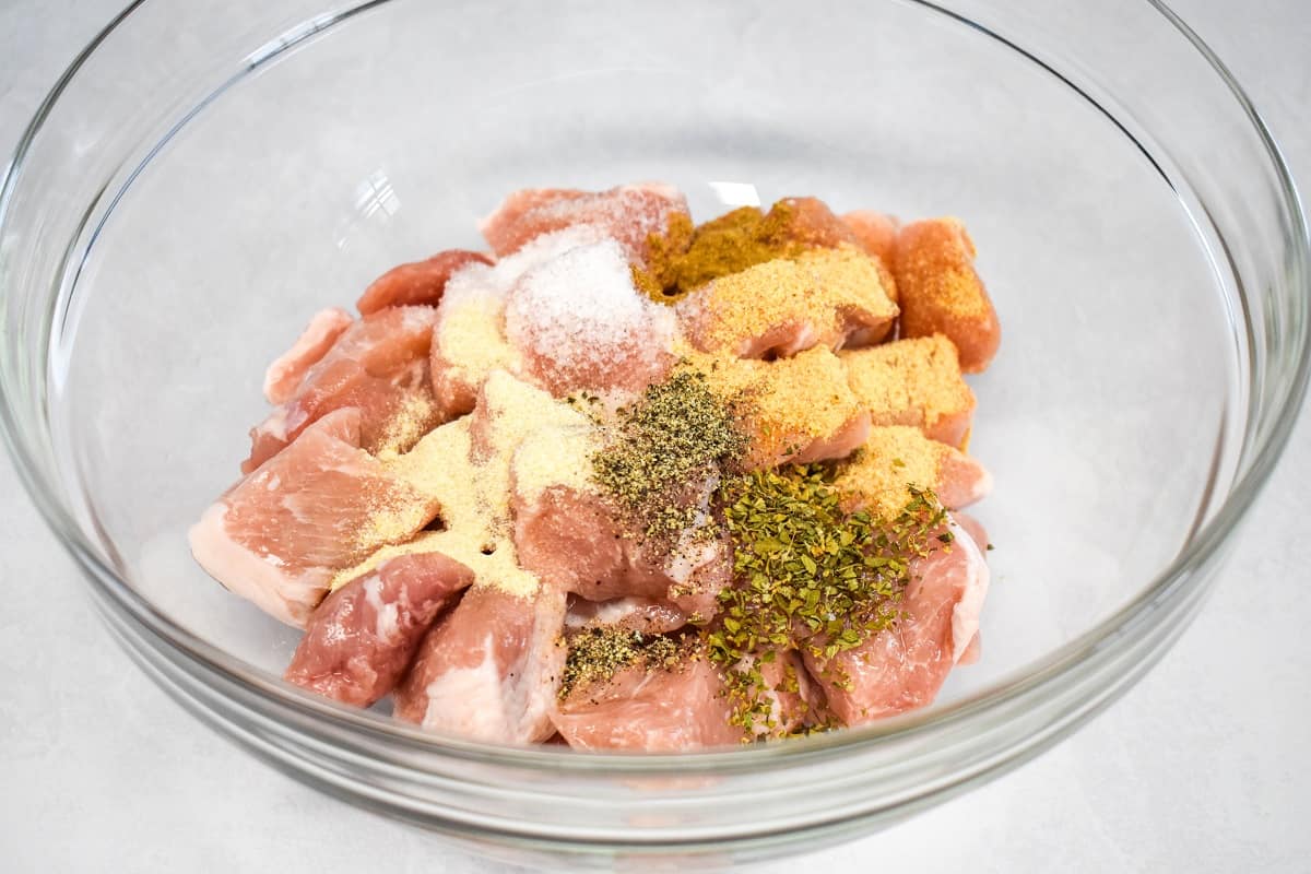 The meat chunks in a large, glass bowl with the seasoning on top.