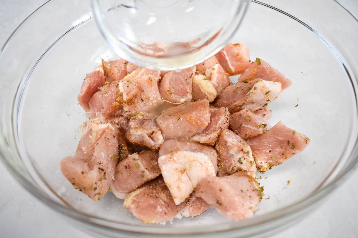 The meat in a large, glass bowl, seasoned with lime juice being poured on it.