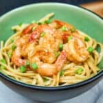 Shrimp sesame noodles in a green bowl, garnished with sliced green onions and sesame seeds, on a gray linen.