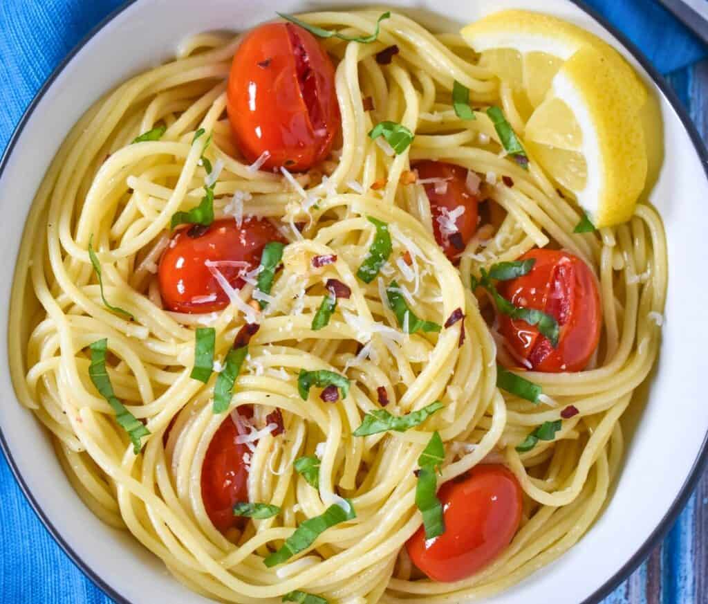The finished spaghetti aglio e olio with tomatoes and basil served in a white bowl.