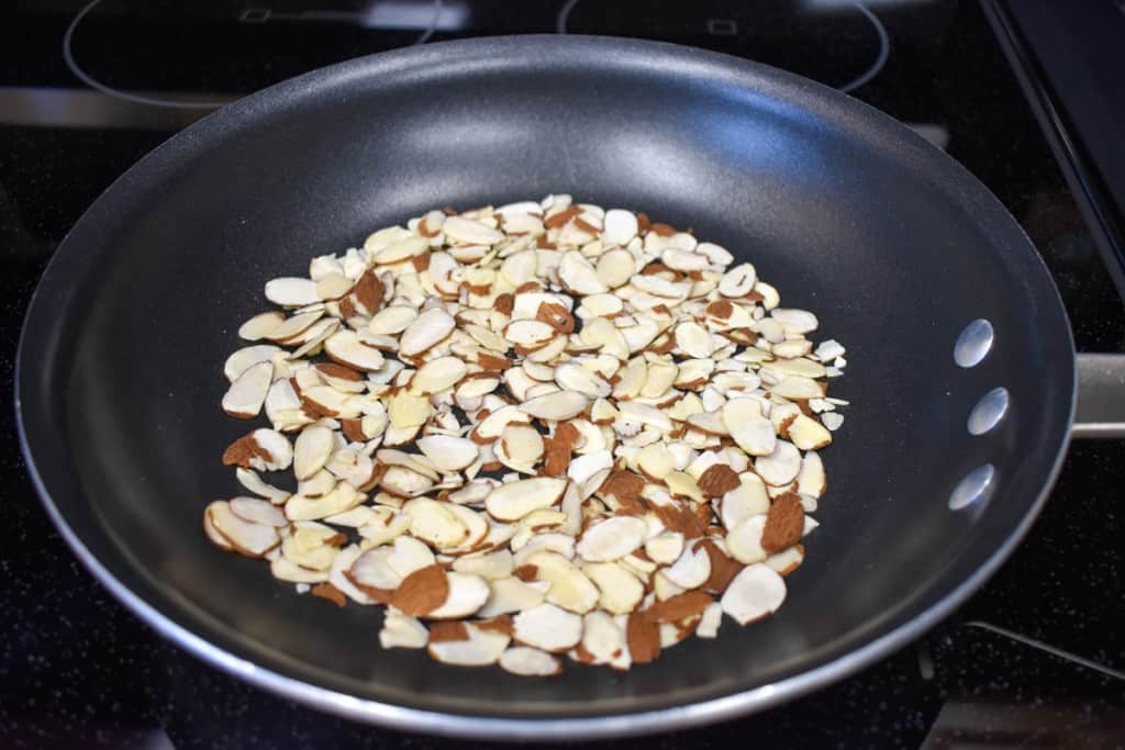 An image of sliced almonds in a non-stick skillet.