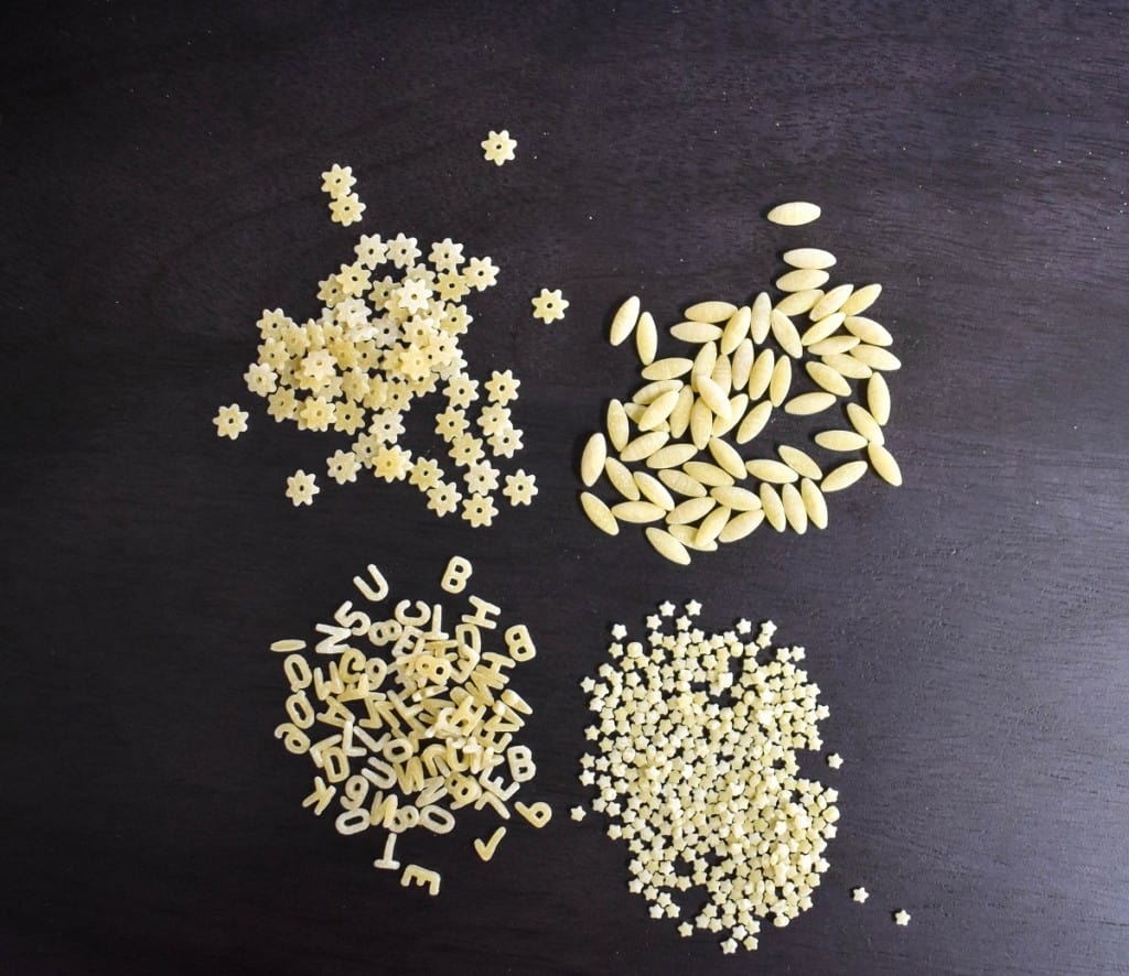 An image of four types of pastina displayed on a dark brown board.