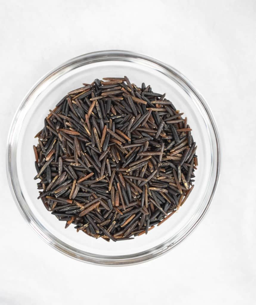 An image of uncooked wild rice displayed in a clear bowl on a white table.