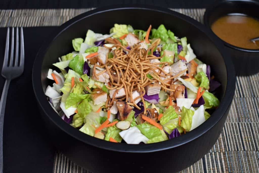 Asian Chopped Salad, topped with crunchy rice noodles, sliced almonds, and chopped grilled chicken served in a black bowl.