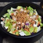 Asian Chopped Salad, topped with crunchy rice noodles, sliced almonds, and chopped grilled chicken served in a black bowl.