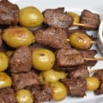 Beef & Potato Skewers served on a white platter with chimichurri sauce on the side