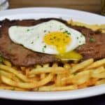 Bistec a Caballo a thin, pan fried steak served on a bed of fries and topped with a fried egg with the yolk pierced and running into the fries