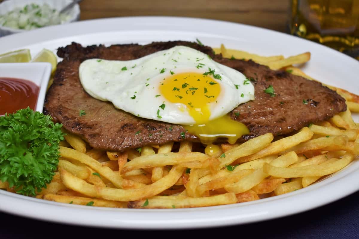 Bistec a Caballo a thin, pan fried steak served on a bed of fries and topped with a fried egg with the yolk pierced and running into the fries