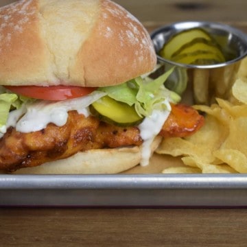 Buffalo Chicken Sandwich served with lettuce, tomato, pickles, and blue cheese dressing on a bun with a side of chips