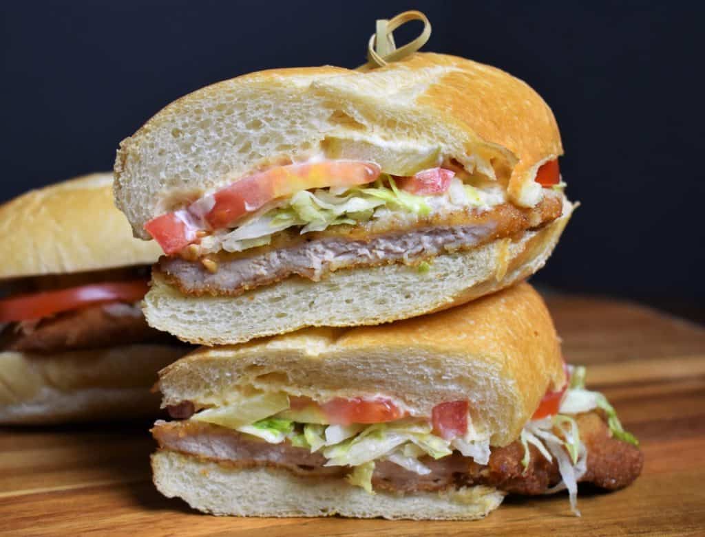 Fried Pork Sandwich, served on a sub roll with shredded lettuce, tomatoes and mayo, cut in half and stacked.
