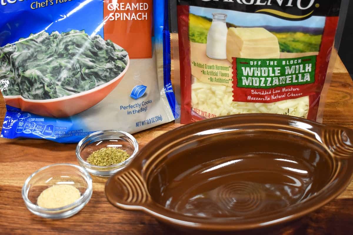 The ingredients for the hot spinach dip in their packages displayed on a wood cutting board.