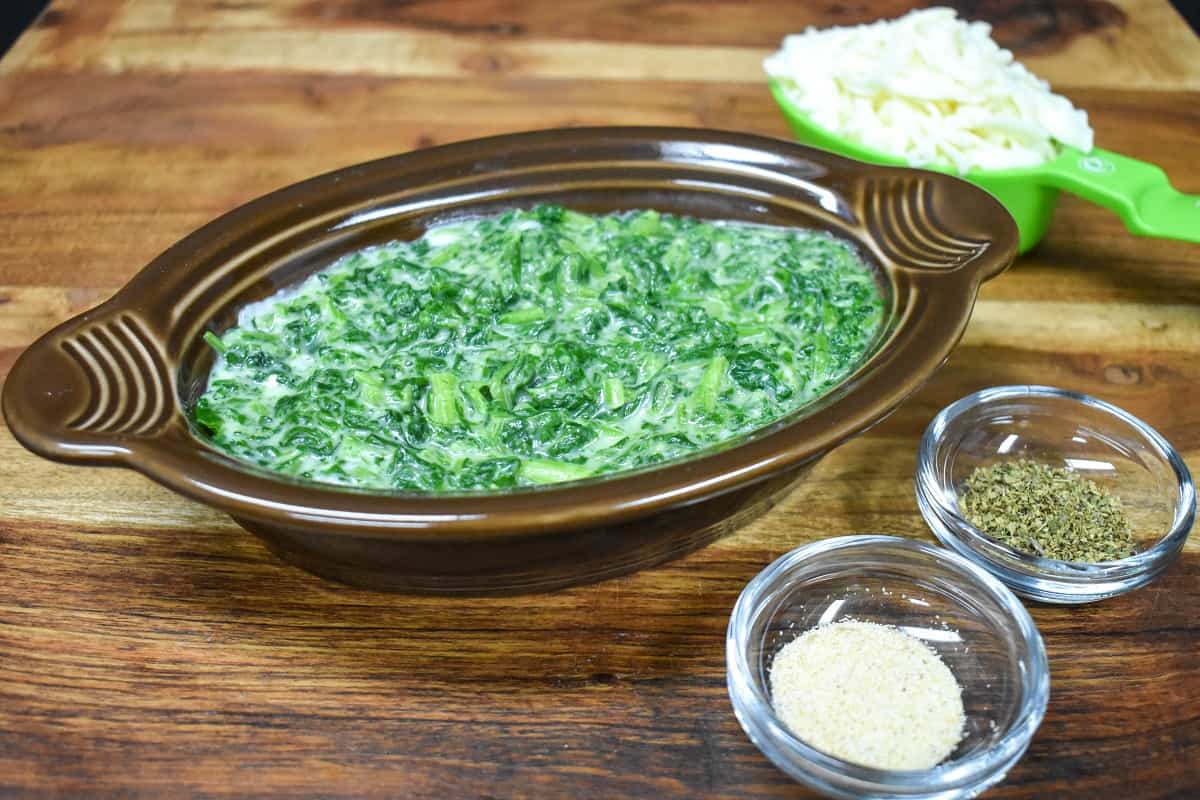 Creamed spinach in a brown bowl displayed on a wood cutting board.