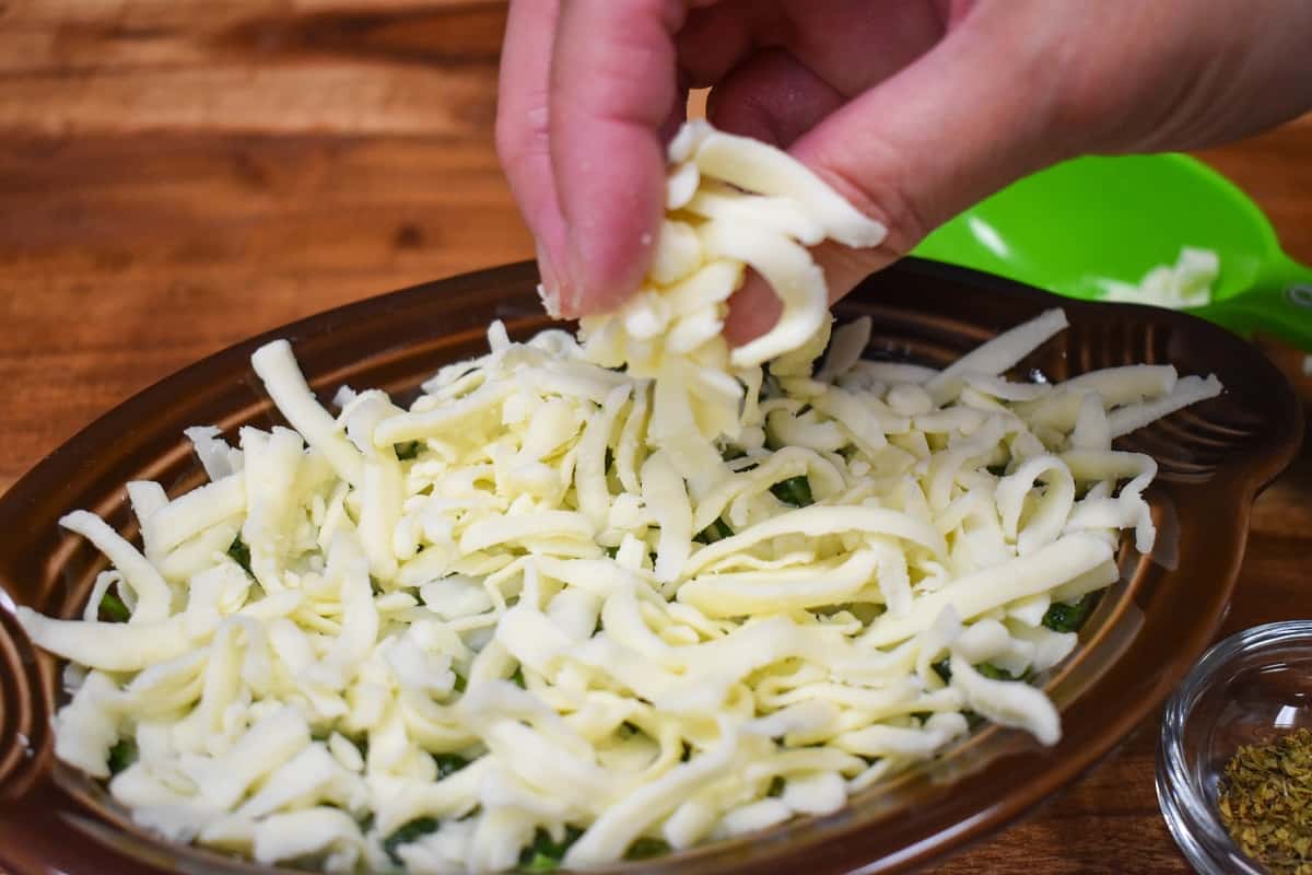 Shredded mozzarella cheese being sprinkled on creamed spinach.