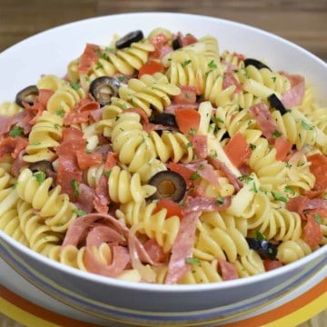 Italian Pasta Salad, rotini pasta with sliced salami, provolone cheese, sliced olives served in a white bowl