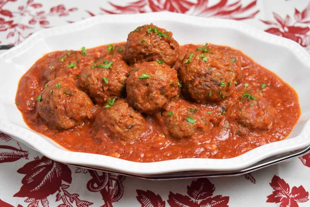 Meatballs Cuban Style served on a white platter in a red sauce and garnished with chopped parsley