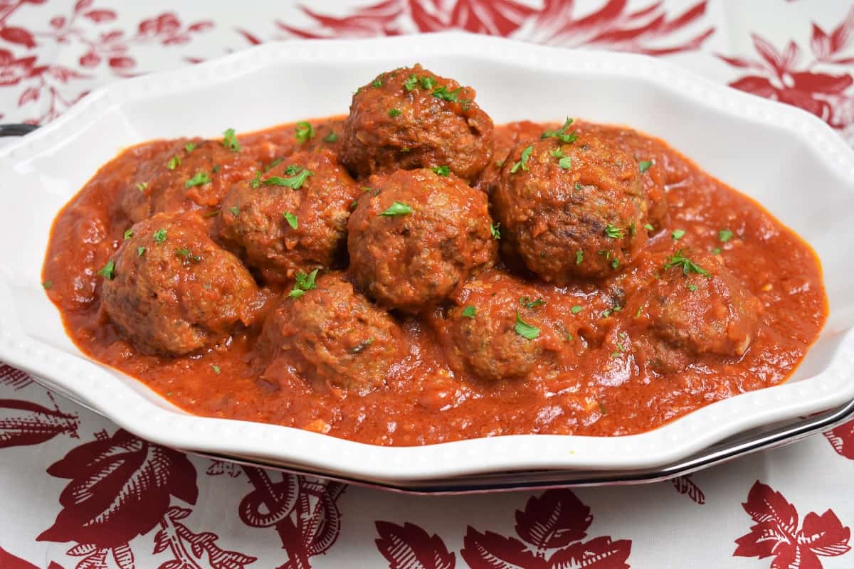 Meatballs Cuban Style served on a white platter in a red sauce and garnished with chopped parsley