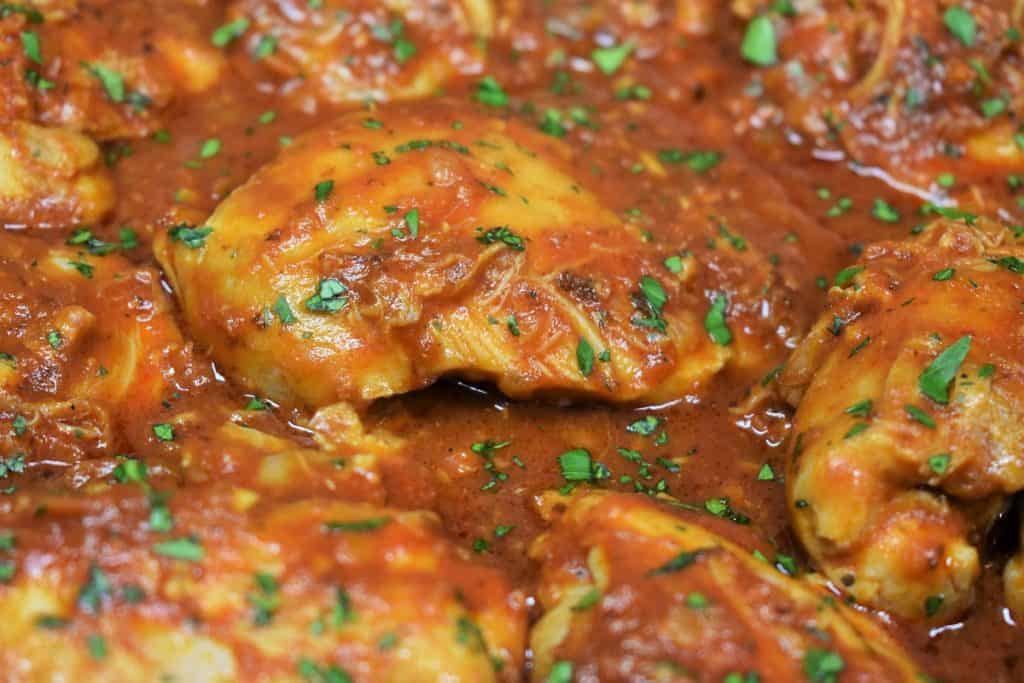 A close up picture of chicken in red sauce, garnished with parsley