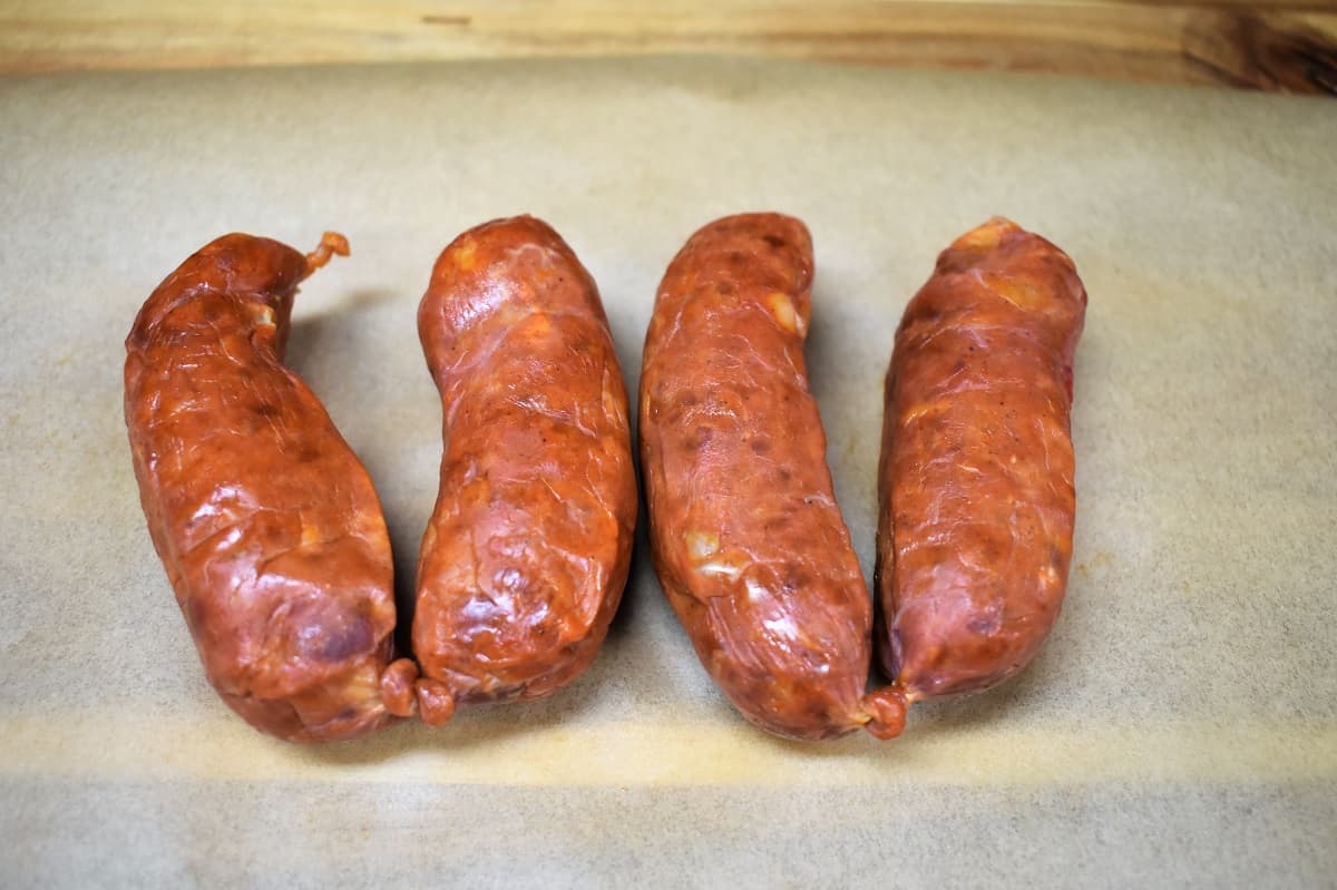 Four Spanish Chorizo Links on parchment paper displayed on a wood cutting board
